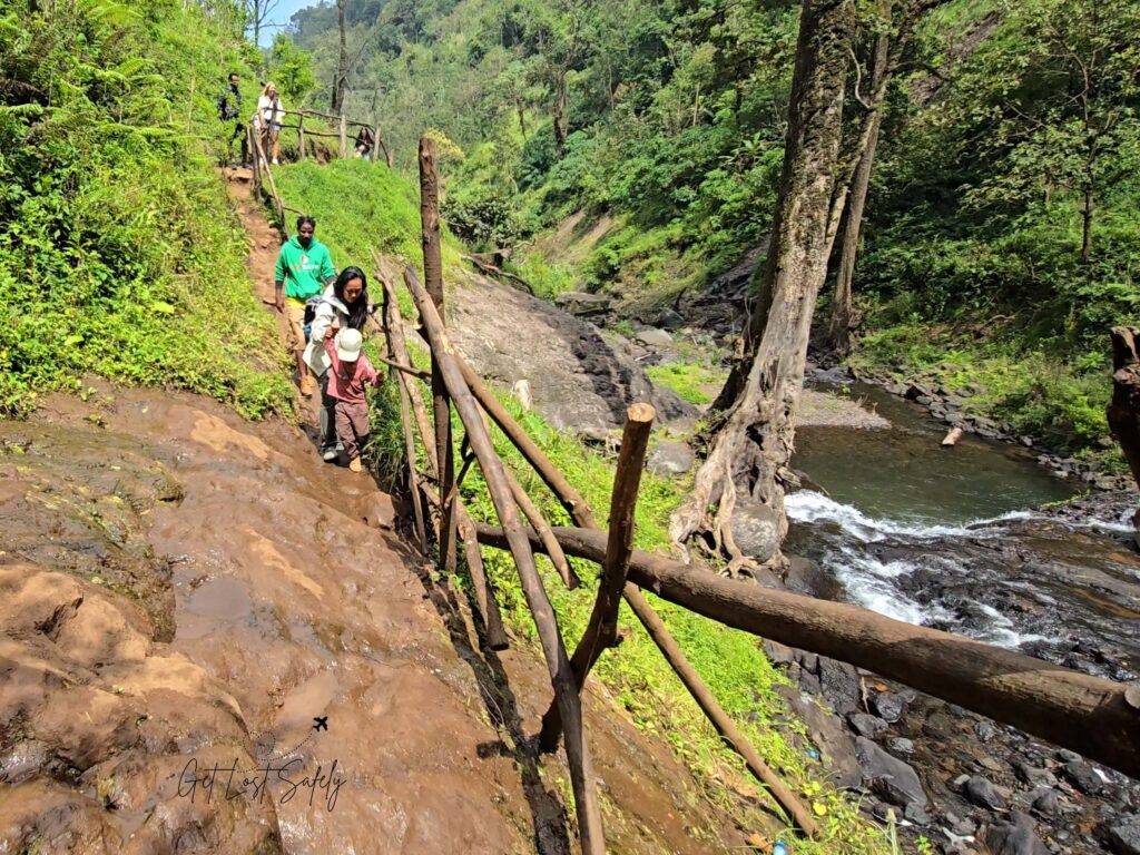Steep and slippery hike to Materuni Waterfalls. Kid and his mom with other tourists walking on a stone and wooden fence to 80 m waterfall in Materuni Village, Tanzania.
