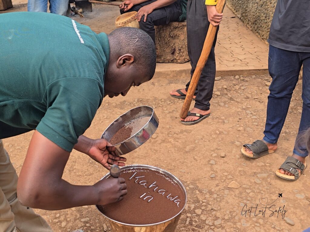 The guide is writing the word Kahawa on the top of freshly roasted, and grinded coffee, which means coffee in local language.
